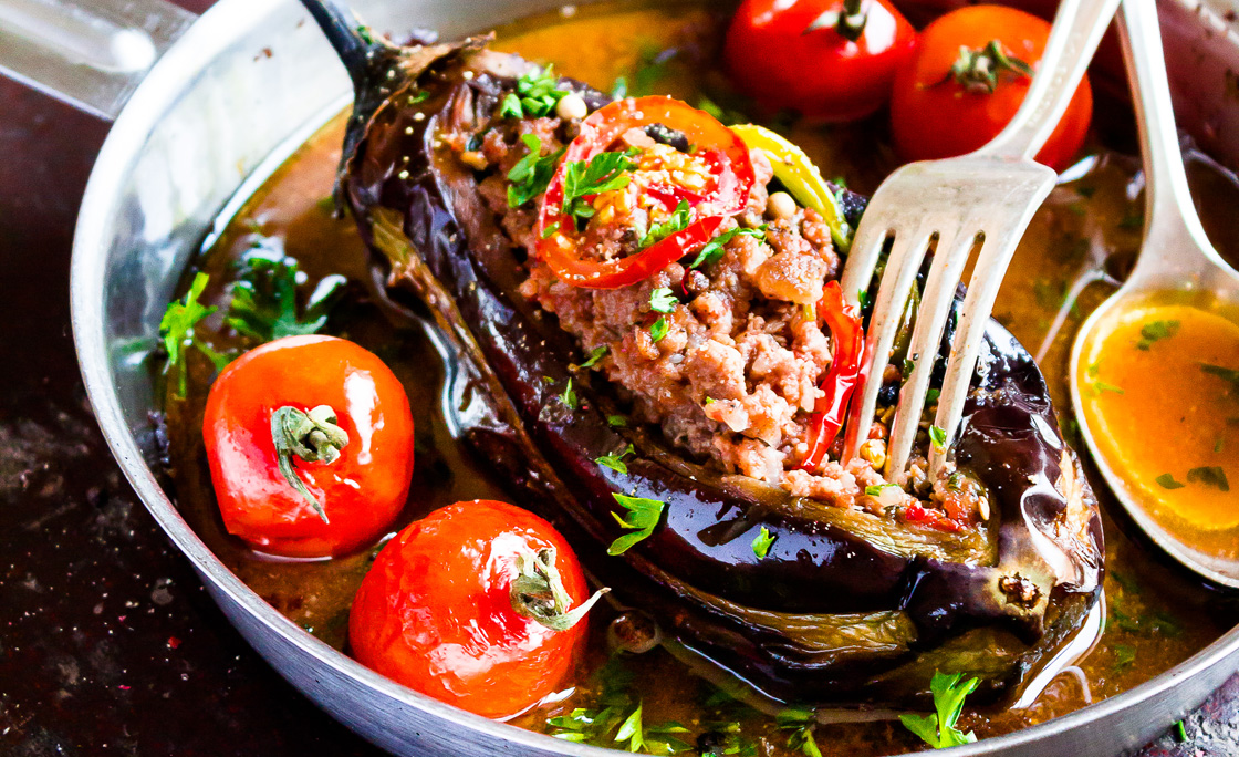 Baked aubergine or eggplant stuffed with minced pork and beef, carrot, pepper, cherry tomatoes in a pan on a wooden table, selective focus