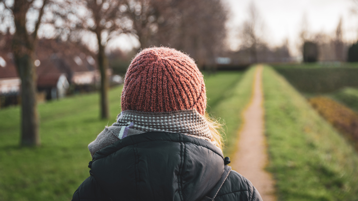 Woman walking on a narrow path dressed in warm clothes from behind