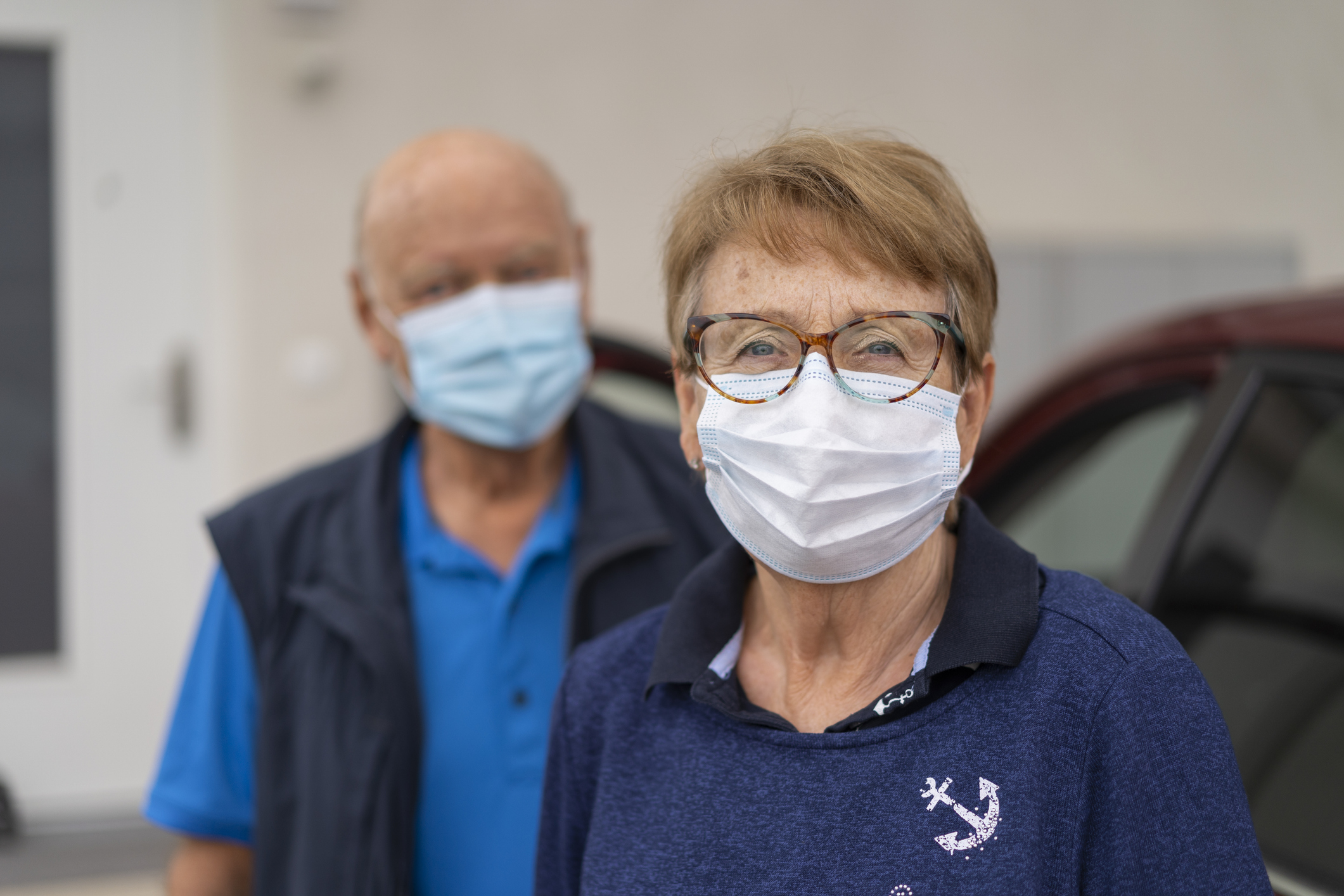 smiling senior woman with mask, senior man husband blurred in background