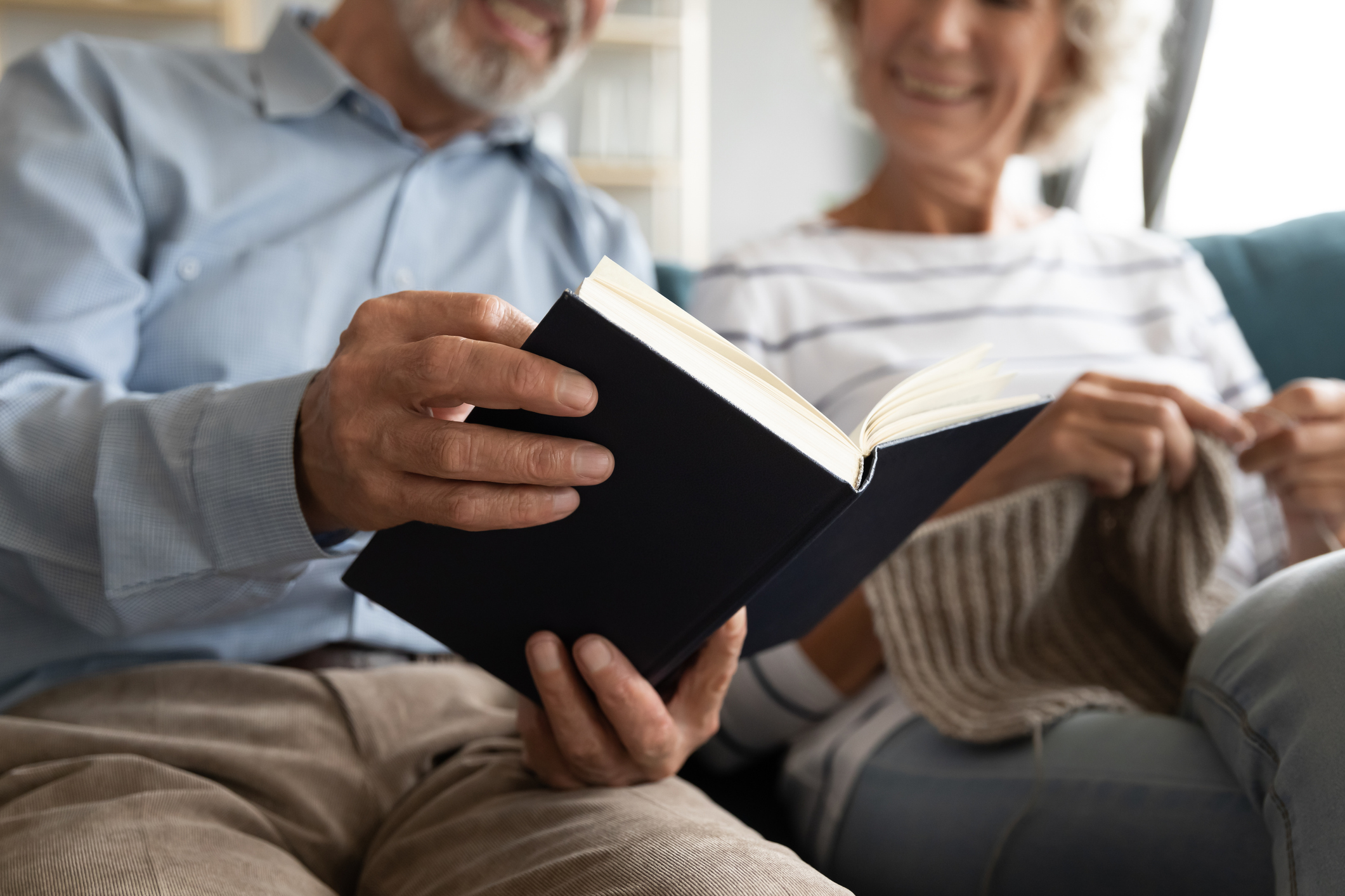 Happy older husband reading book while wife knitting