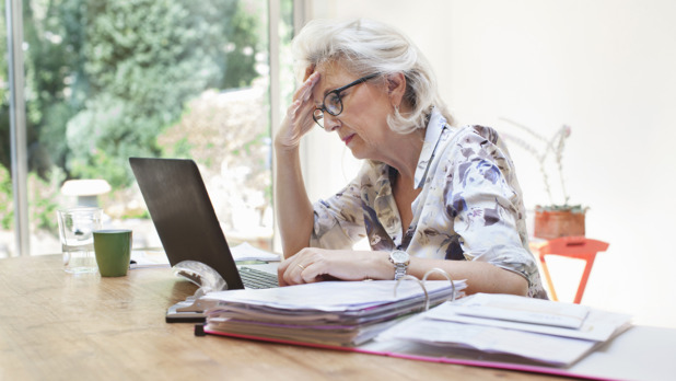Senior woman sitting at table, using laptop, worried expression
