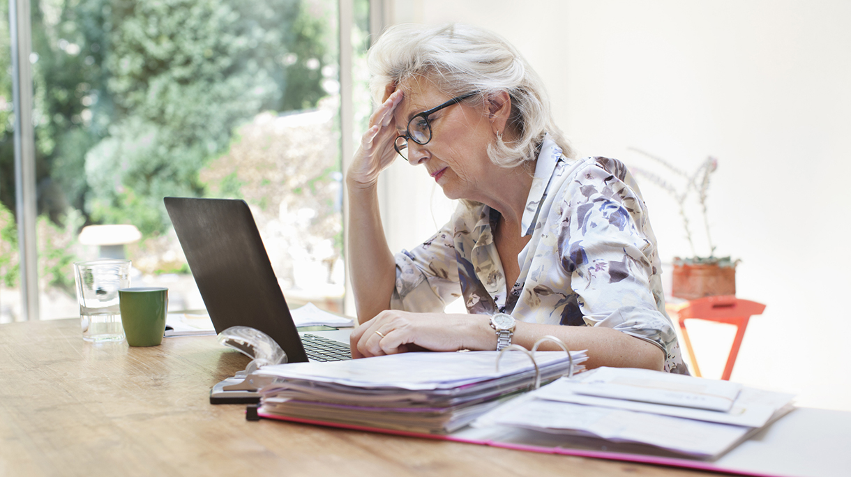 Senior woman sitting at table, using laptop, worried expression