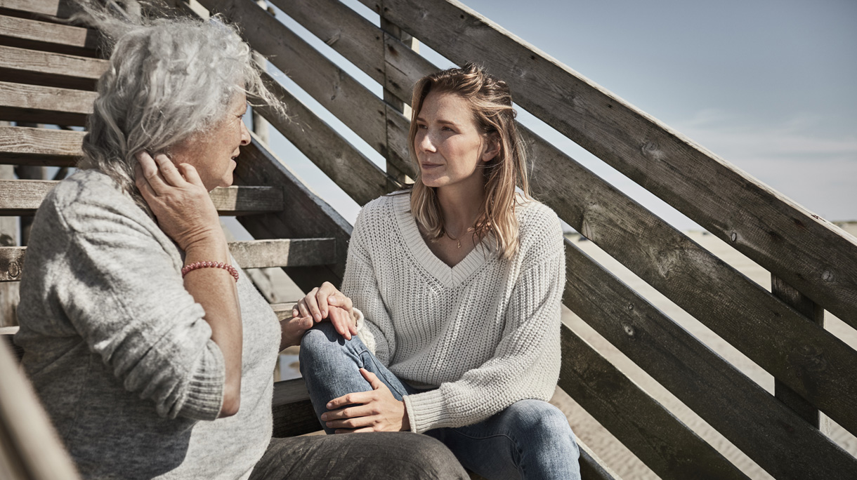 Senior woman talking with adult daughter on footbridge at the beach