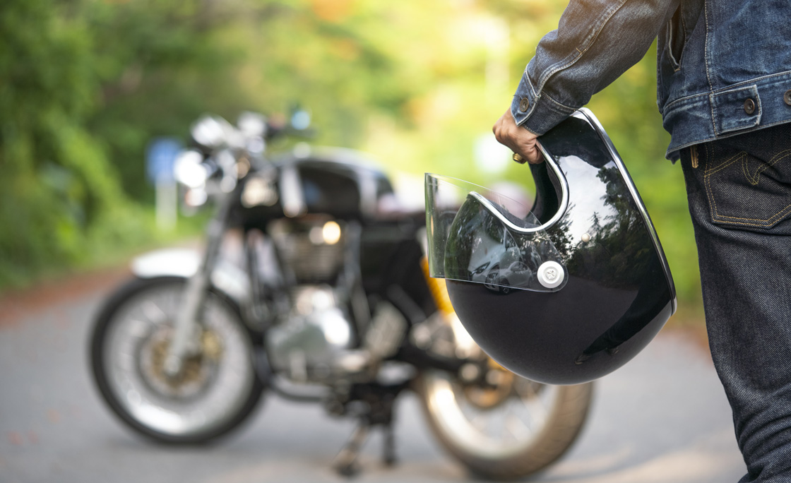 Handsome man in jean is holding a helmet and vintage motorcycle blur background