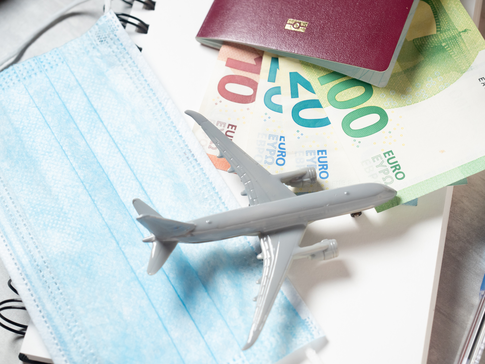 Protective mask, toy plane, passport and money on the table