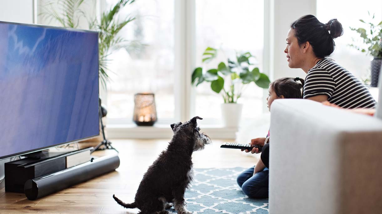 Mother and daughter watching television while sitting with dog on floor at home