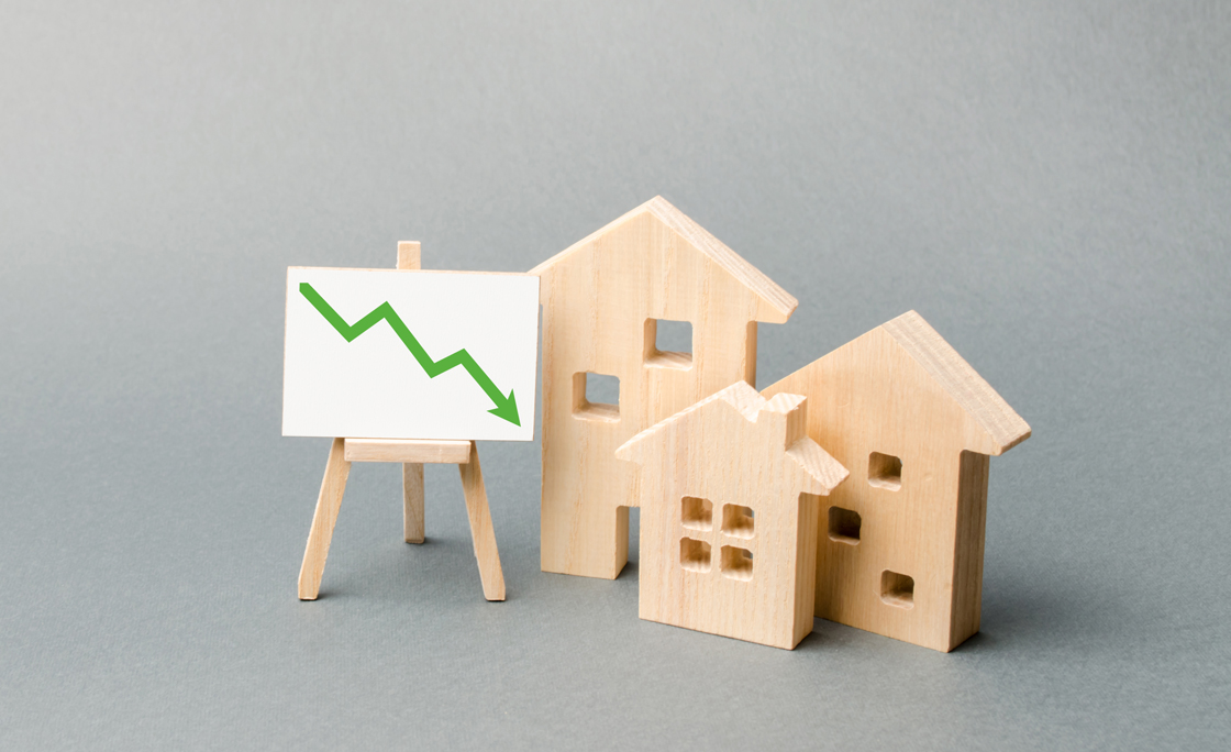 Wooden houses and an easel arrow down. The fall of the real estate market. concept of value or cost decrease. low liquidity and attractiveness. cheap rent. Reduced demand and market stagnation.
