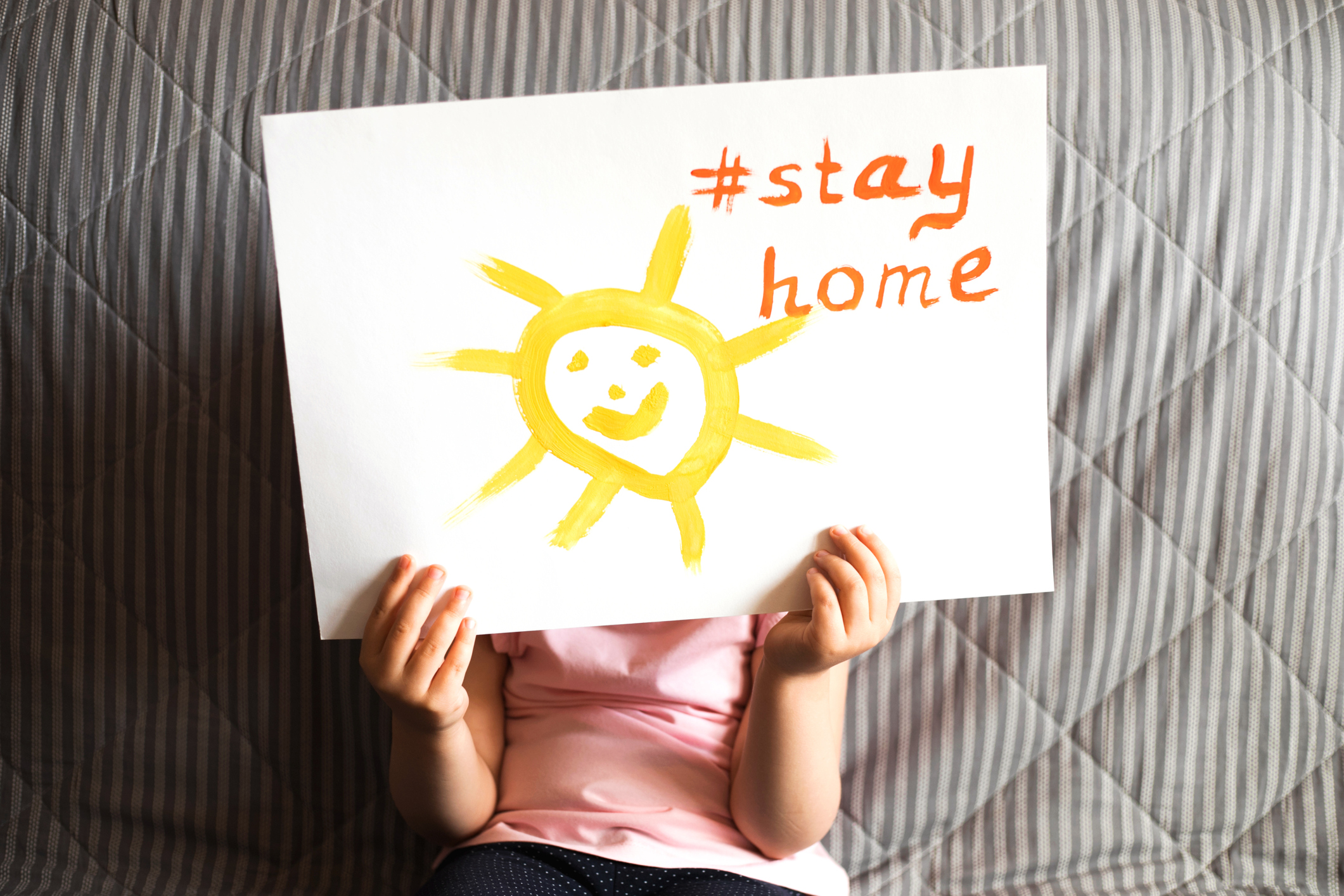 Close up of child’s hands holding a piece of paper with text Stay Home and sun.