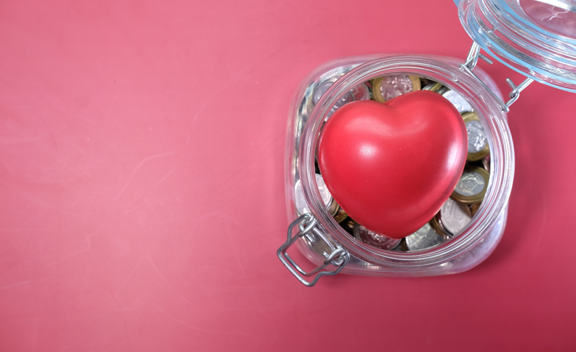 Top View Of Heart Shape Symbol And Coins In Jar On Table.