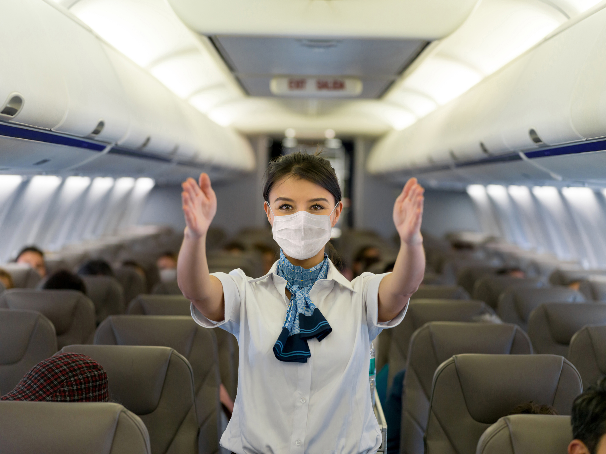 Flight attendant showing the emergency exit in an airplane wearing a facemask