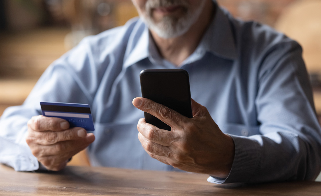 Close up mature man using phone, holding plastic credit card