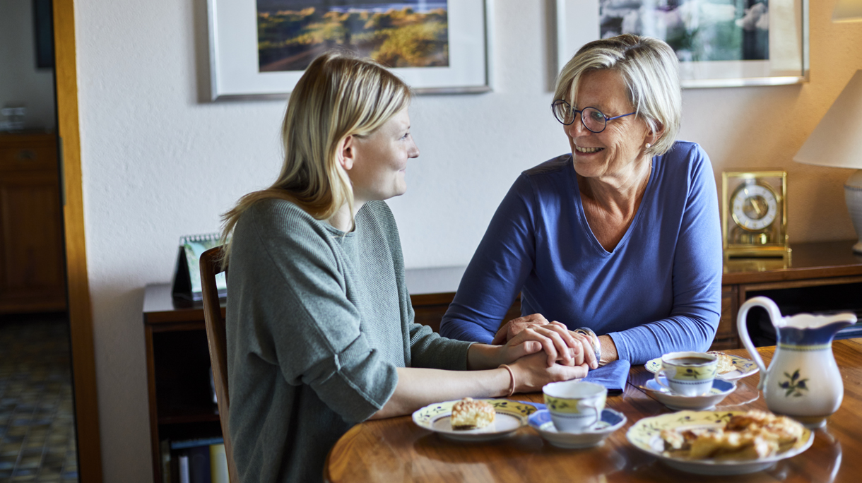 Senior woman and young woman sitting at dining table holding hands