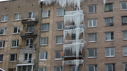 Huge icicles hang from the balconies of a residential building. Harsh winter. Utilities do not cope. Dangerous stalactites. Terrible ice in the big city.
