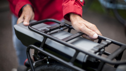 Midsection of senior woman inserting battery in backseat of electric bicycle