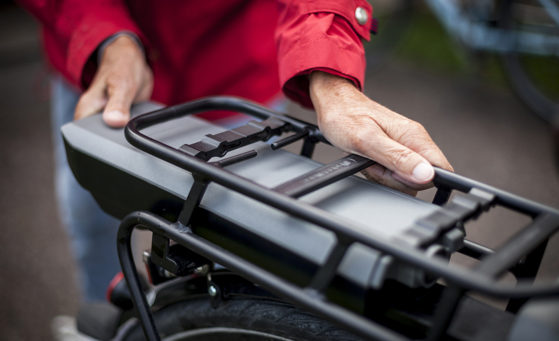 Midsection of senior woman inserting battery in backseat of electric bicycle