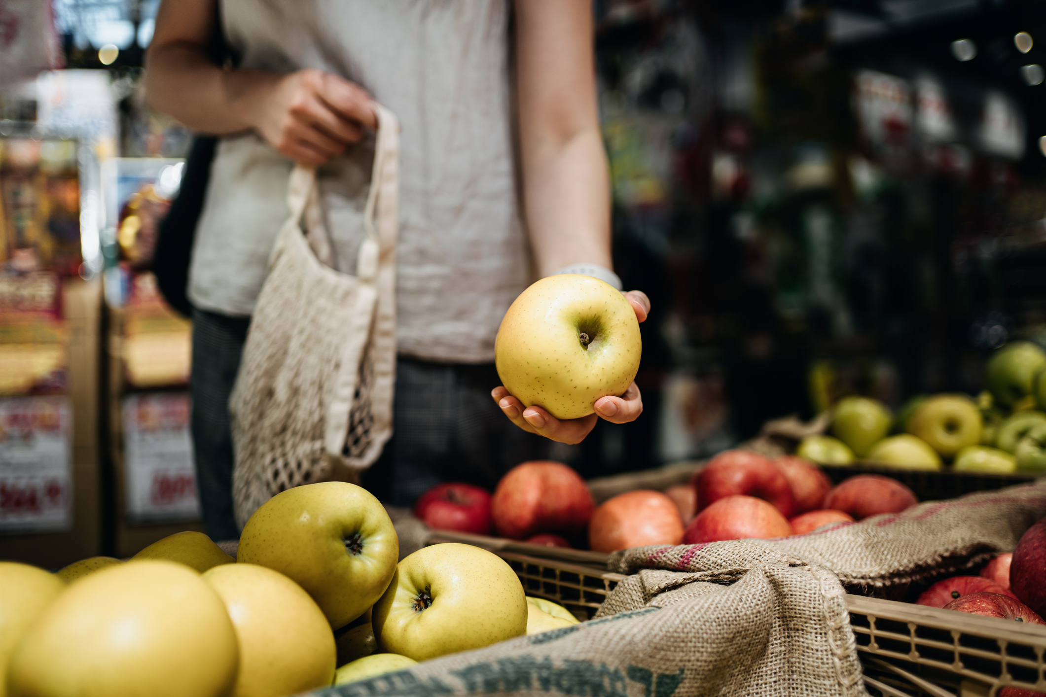 Close up of young Asian woman shopping for fresh organic fruits in farmer’s market with a cotton mesh eco bag. Environmentally friendly and zero waste concept
