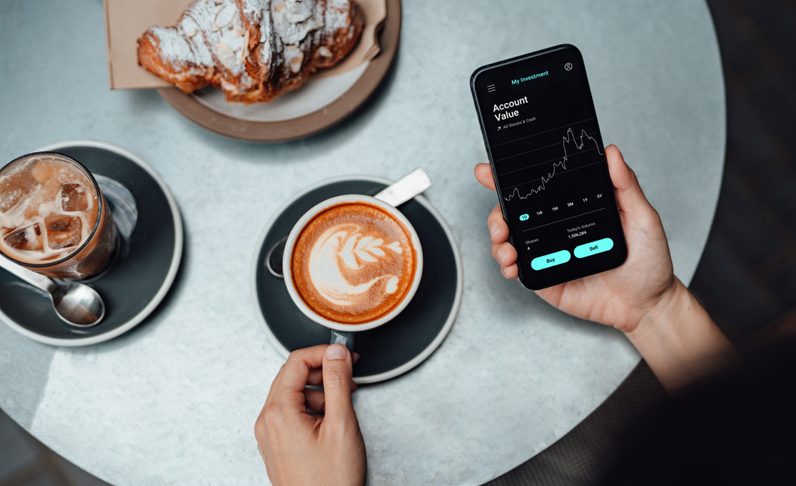 Young Woman Using Stock Trading App On Smart Phone At Cafe