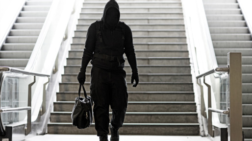 Hooded Lone wolf Man wearing black carrying bag in urban underground public transport setting