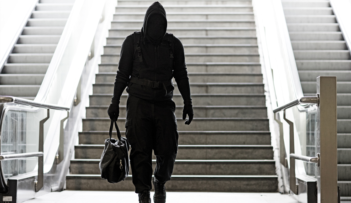 Hooded Lone wolf Man wearing black carrying bag in urban underground public transport setting