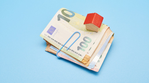Still life of a bundle of Euro bank notes and small red house on blue background
