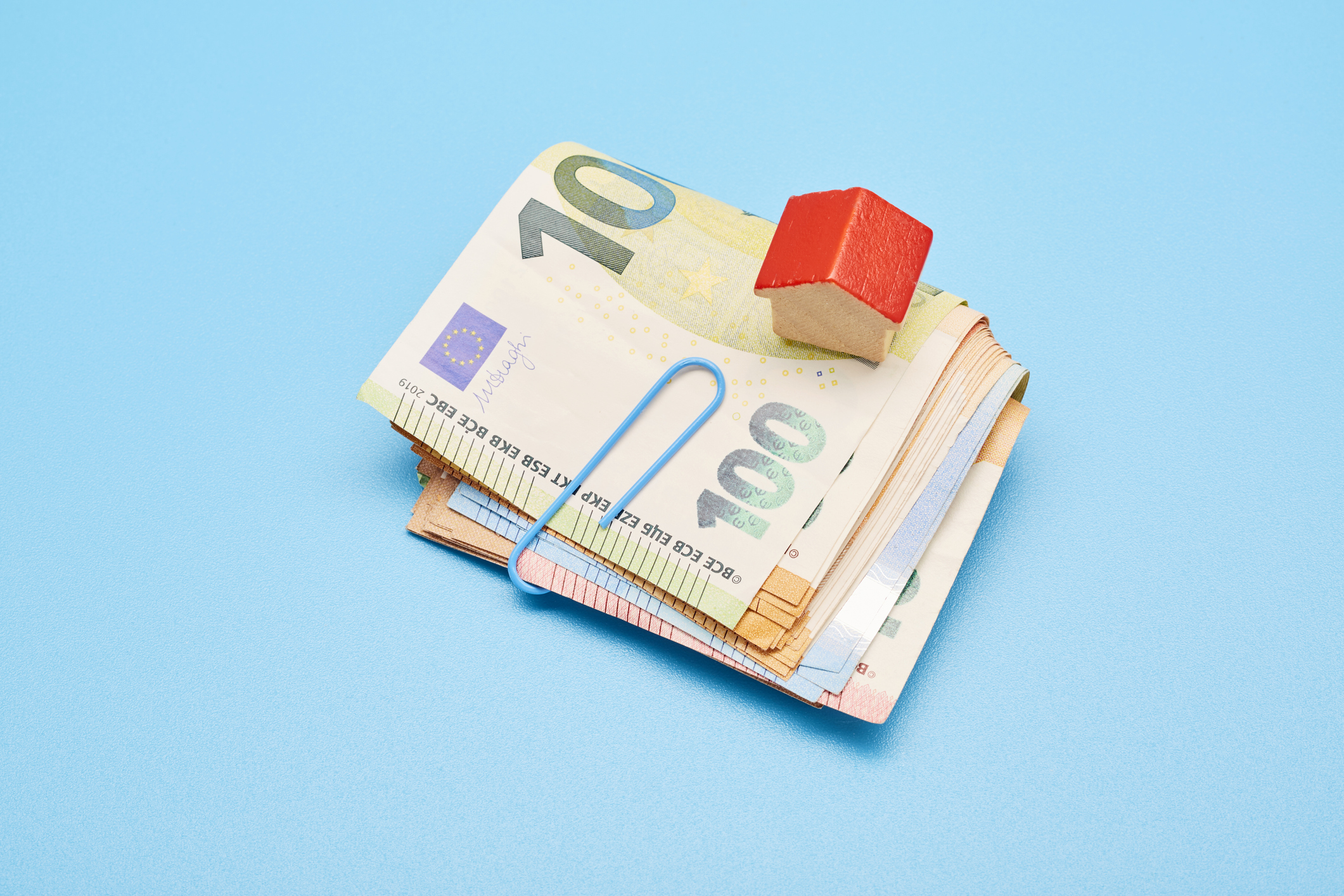 Still life of a bundle of Euro bank notes and small red house on blue background
