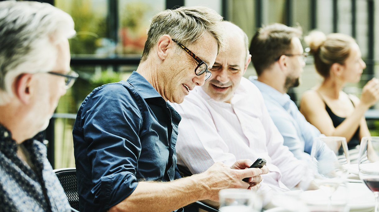 Smiling friends looking at smartphone during dinner on restaurant patio