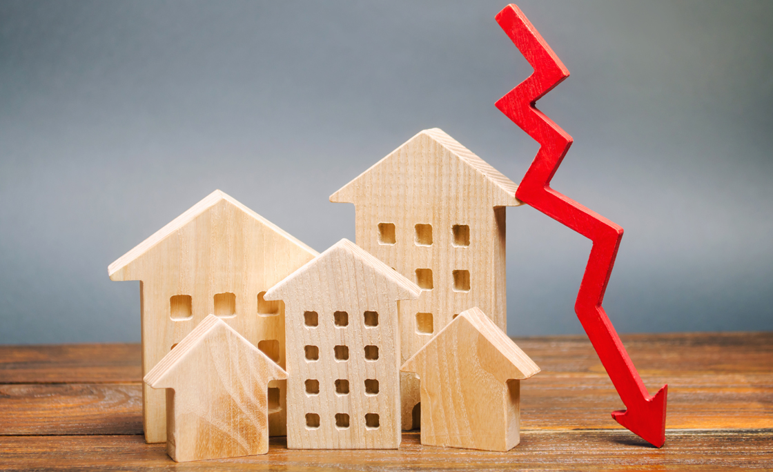 Miniature wooden houses and a red arrow down. The concept of low cost real estate. Lower mortgage interest rates. Falling prices for rental housing and apartments. Reducing demand for home buying
