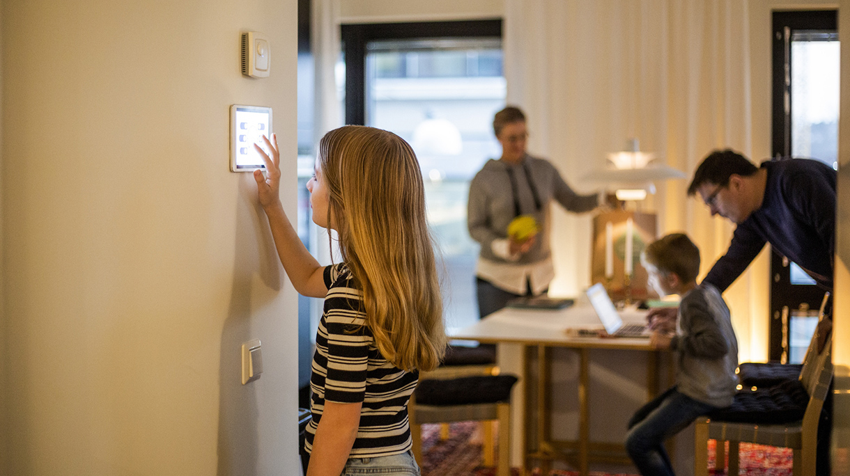 Girl using digital tablet on wall with family in background at smart home