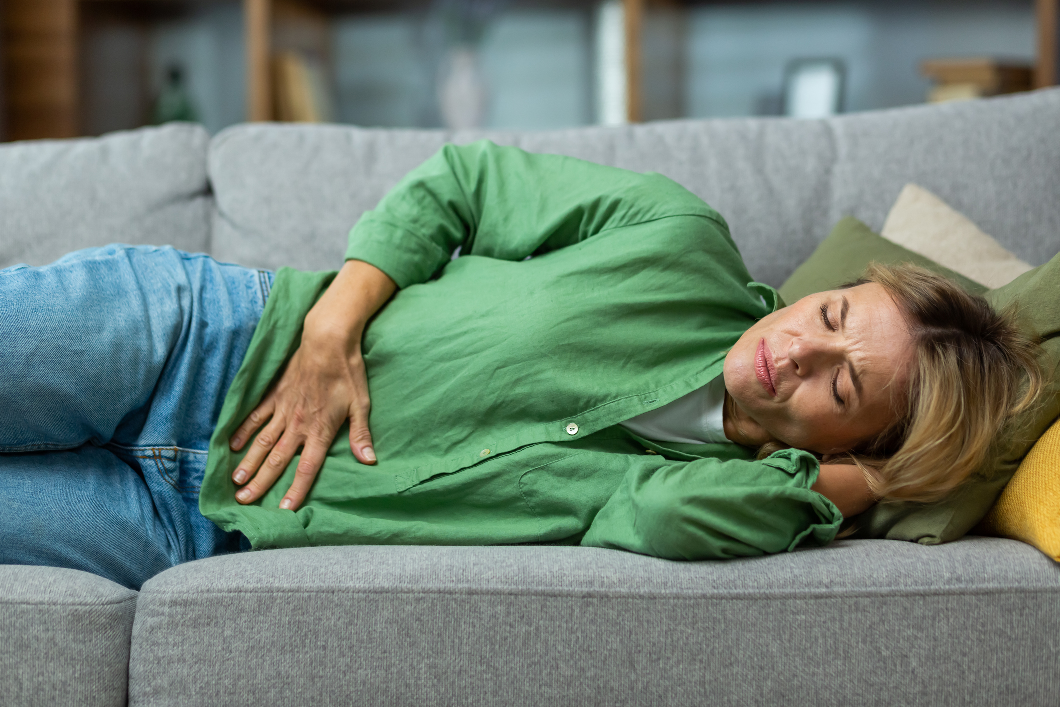 Norovirus buikpijn vrouw ligt op de bank met handen op buik