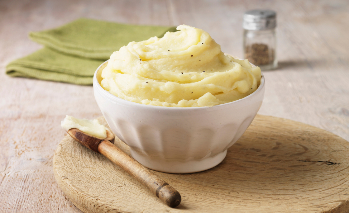 Ultimate mashed potato with black pepper in white faceted bowl with wooden spoon