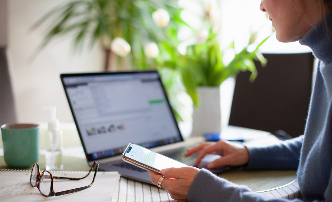Woman working from home using laptop computer while reading text message on mobile phone