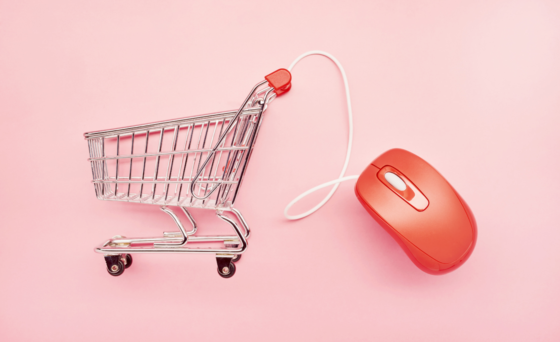 Still life of a small shopping cart and red computer mouse on pink background, online shopping