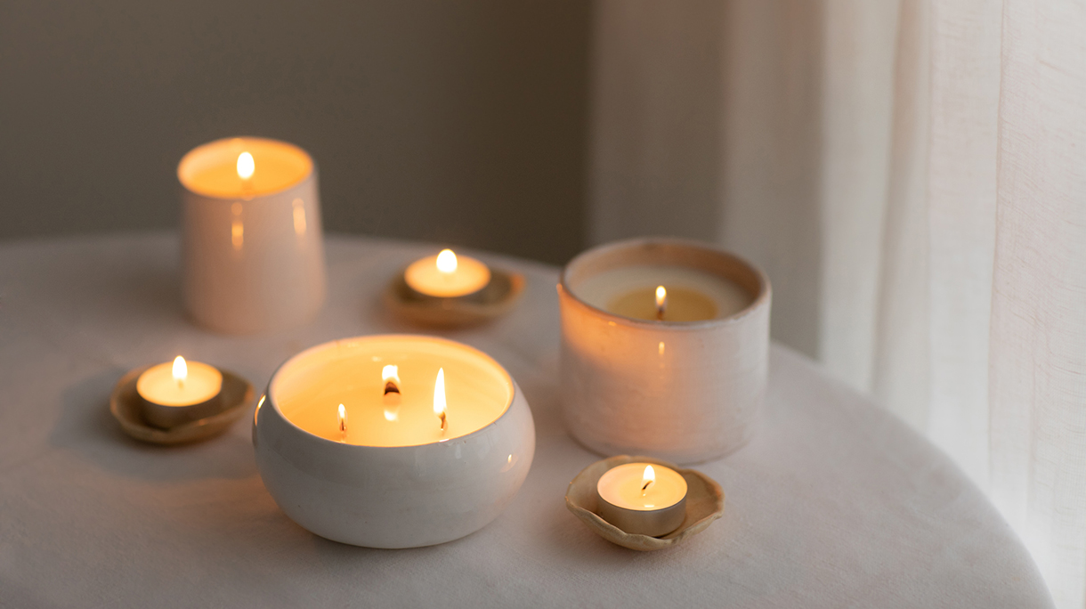 Scented candles in ceramic bowls on linen tablecloth at home.