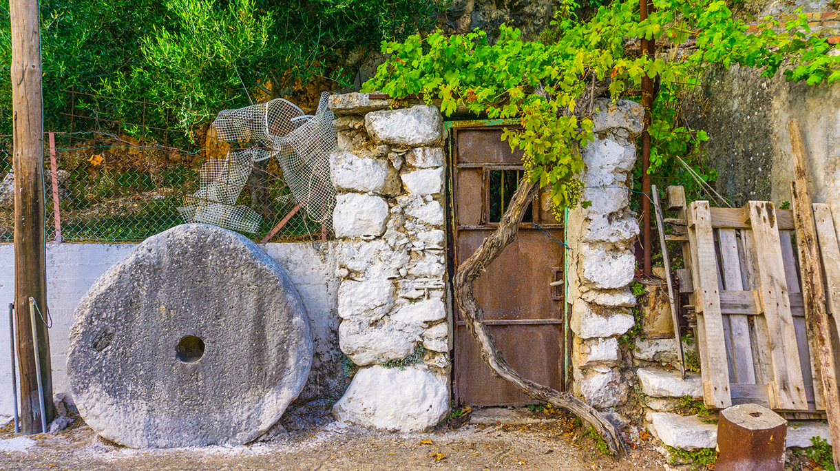 An old abandoned rusty door of a house and a millstone at Arginia, a remote village in mountain Ainos in the southern side of Cephalonia island in Greece