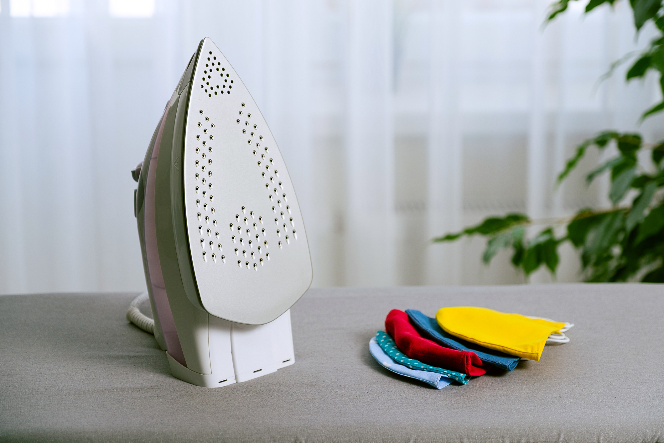 Iron and reusable fabric stitched masks on the ironing board. Prevention and protection against infection with influenza viruses, covid-19. Decontamination, disinfection and sterilization of masks for reuse.