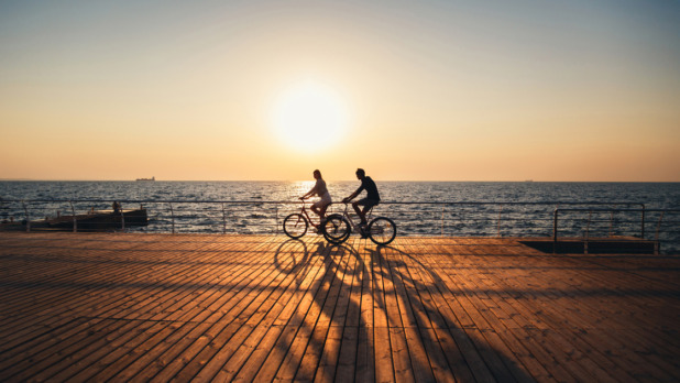 Couple of young hipsters cycling together at the beach at sunrise sky at wooden deck summer time