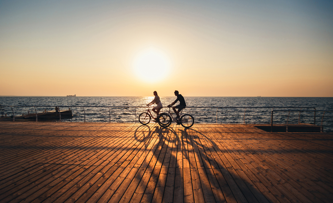 Couple of young hipsters cycling together at the beach at sunrise sky at wooden deck summer time