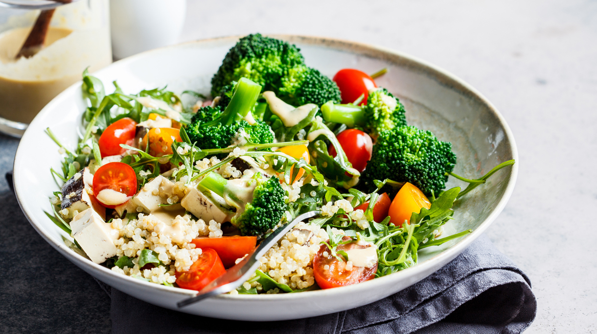 Vegan quinoa salad with tofu, broccoli, tomatoes and nutty dressing. Healthy food concept.