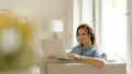 Mature woman sitting on couch at home using laptop