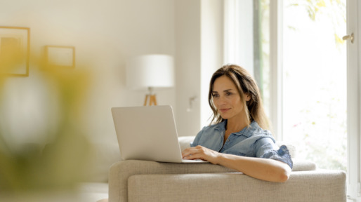 Mature woman sitting on couch at home using laptop