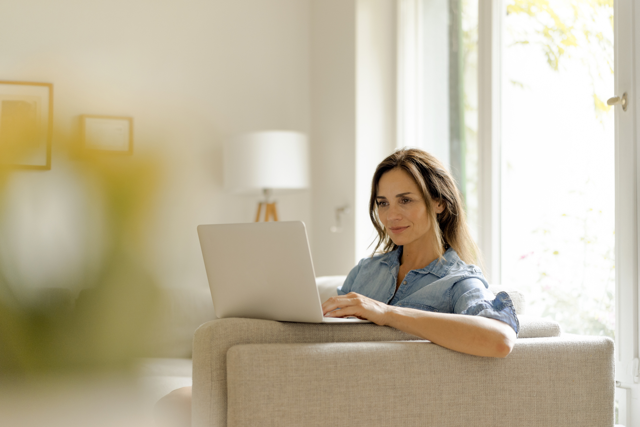 Mature woman sitting on couch at home using laptop