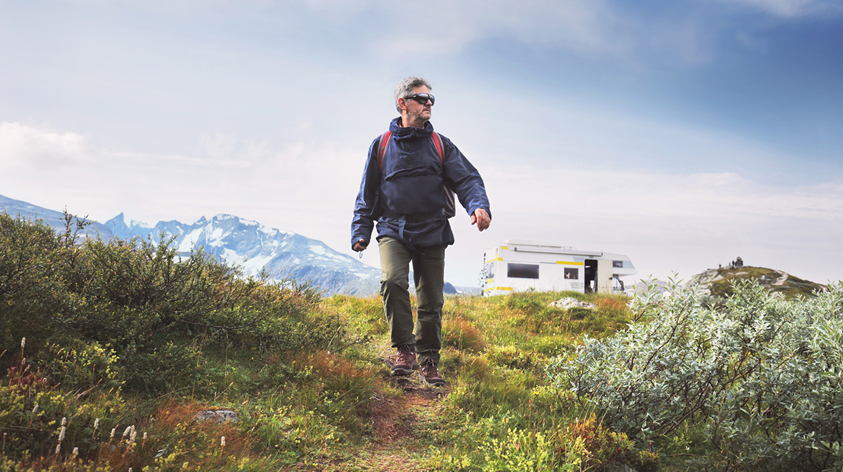 Senior man traveling with backpack, campervan and mountains in background