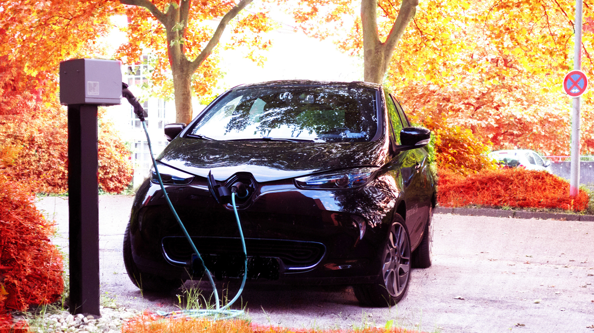 Electric Car Charging On Road Against Autumn Trees