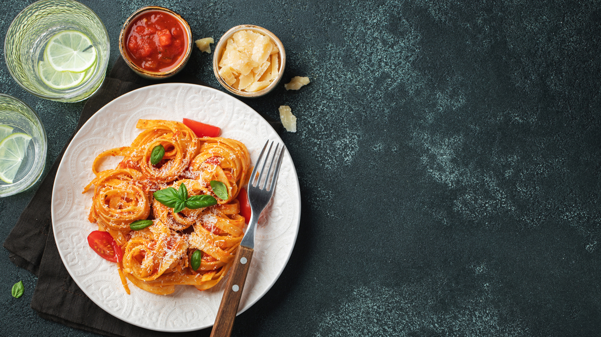 Tasty appetizing classic italian tagliatelle pasta with tomato sauce, cheese parmesan and basil on plate on dark table. View from above, horizontal. Top view with copy space