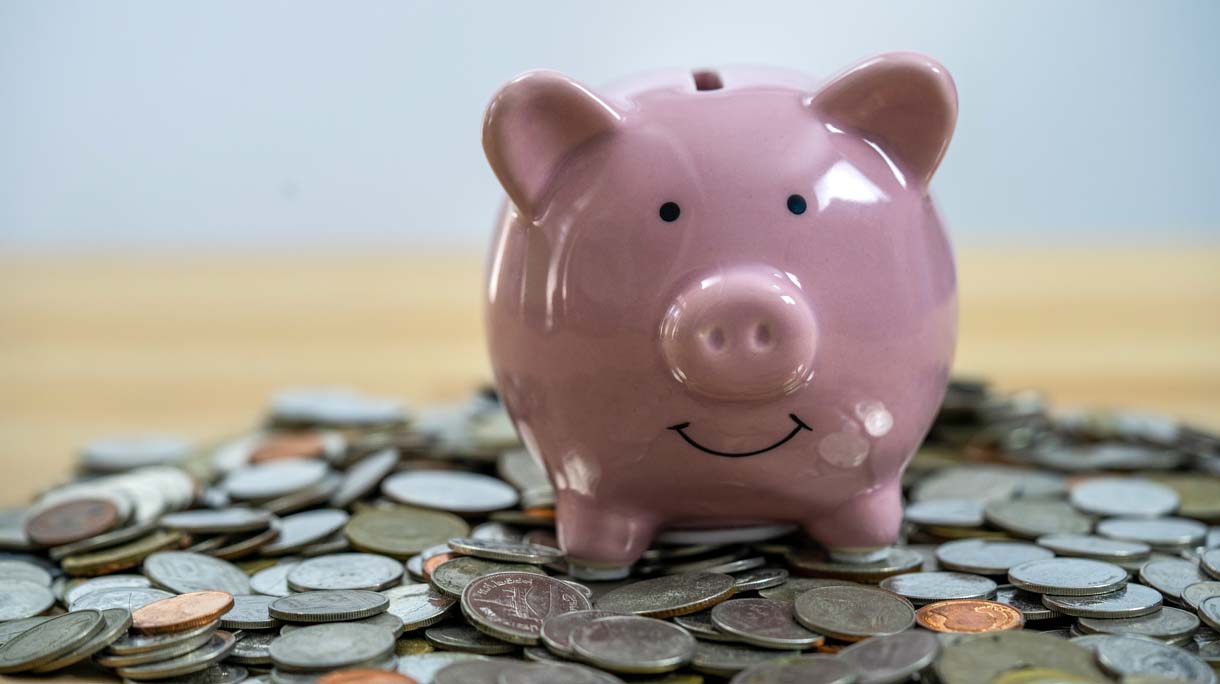 Front view. Pink piggy bank and coins isolated on white