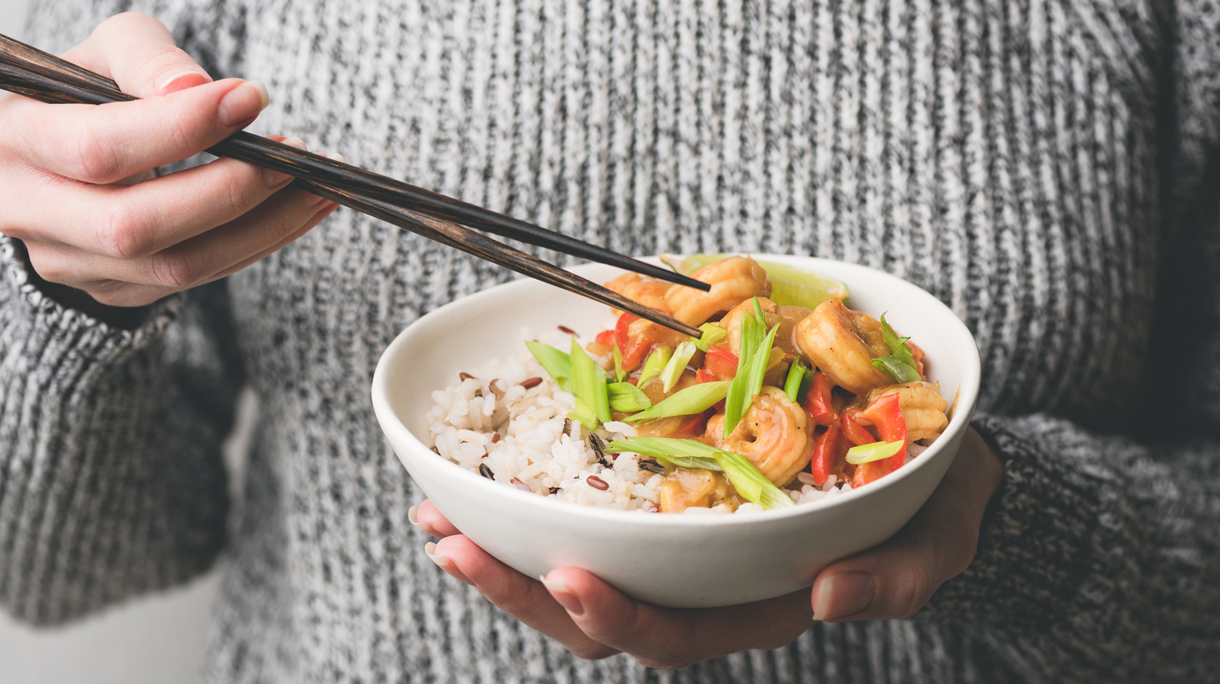 Person eating shrimps with rice using chopsticks