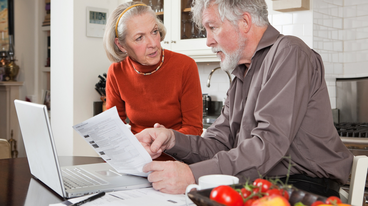 Senior couple looking concerned with bills and laptop