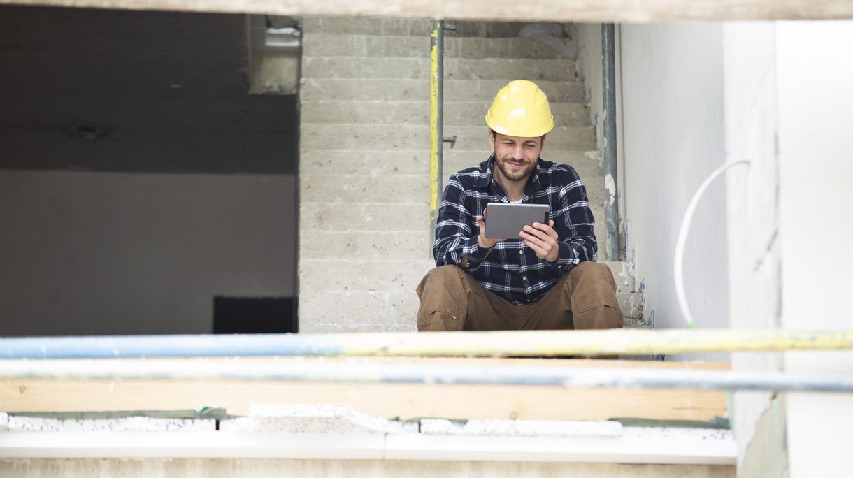 Construction worker using digital tablet while sitting on steps at construction site