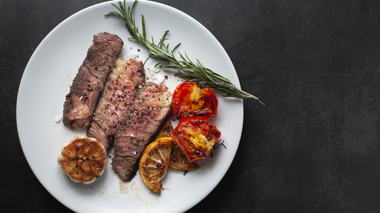 Sliced grilled wagyu steak served on white plate with grilled sliced lemon, tomatoes, garlic and rosemary.