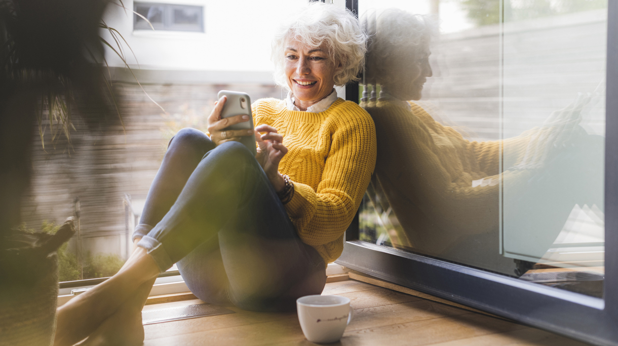 Smiling woman text messaging on smart phone while sitting at home